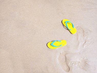 Bej rengi kum yaz plajı arka planında sarı sandaletin en üst görüntüsü. Tatil tatili kavramı.