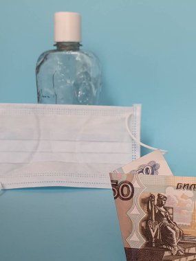 Rus banknotu 50 ruble, yüz maskesi, jel alkollü bir şişe ve mavi arka plan.