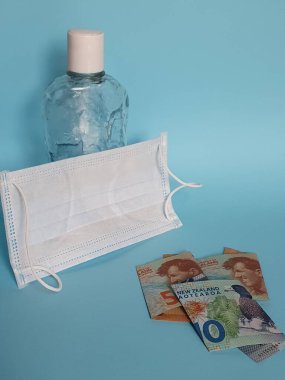 Yeni Zelanda banknotları, yüz maskesi, jel alkollü şişe ve mavi arka plan
