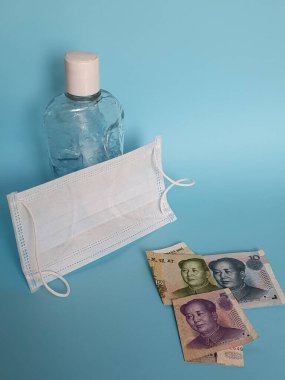 Çin banknotları farklı değerler, yüz maskesi, jel alkollü şişe ve mavi arka plan