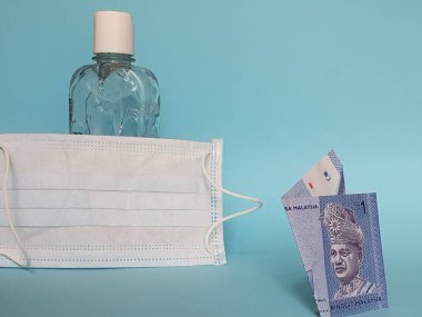 Malezya banknotu bir halka, yüz maskesi, jel alkollü şişe ve mavi arka plan