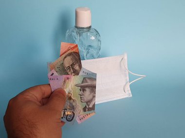 Maske ve bir şişe alkol için Avustralya parasıyla ödeme yapan bir adamın eli.