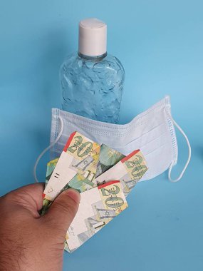 Maske ve bir şişe alkol için İsrail parasıyla ödeme yapan bir adamın eli.