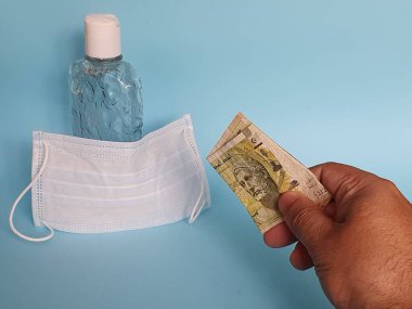 Maske ve bir şişe alkol için Tunus parasıyla ödeme yapan bir adamın eli.