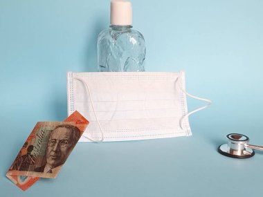 20 dolarlık Avustralya banknotu, maske, jel alkollü şişe ve mavi arka planda steteskop.