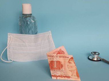 Bir lempira, maske, jel alkollü şişe ve mavi arka planda steteskop.