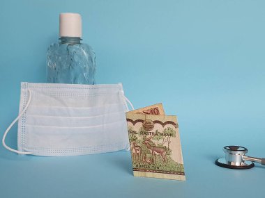 10 rupilik nepal banknot, maske, jel alkollü şişe ve mavi arka planda steteskop.