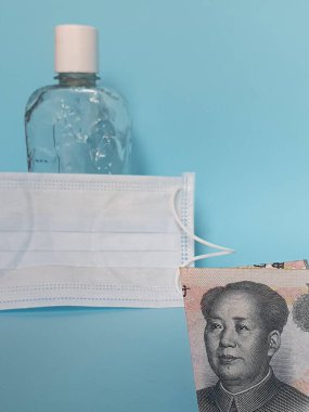 Çin banknotu 10 yuan, yüz maskesi, jel alkollü şişe ve mavi arka plan.