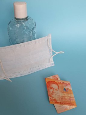 Filipin banknotu 20 peso, yüz maskesi, jel alkollü şişe ve mavi arka plan