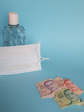 Singapur banknotları, yüz maskesi, jel alkollü şişe ve mavi arka plan