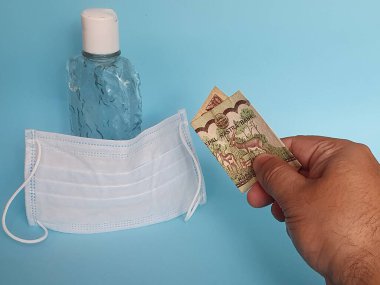 Maske ve bir şişe alkol için Nepal parasıyla ödeme yapan bir adamın eli.