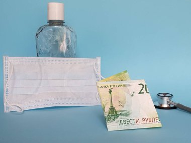200 ruble, maske, jel alkollü şişe ve mavi arka planda steteskop.