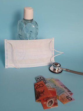 Avustralya banknotları, maske, jel alkollü şişe ve mavi arka planda steteskop.