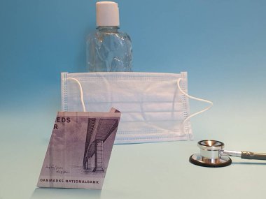 Danimarka banknotu 50 kron, maske, jel alkollü şişe ve mavi arka planda stetoskop.