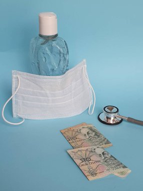 100 korun, maske, jel alkollü şişe ve mavi arka planda steteskop.