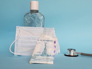 Nikaragua banknotu 100 cordoba, maske, jel alkollü şişe ve mavi arka planda stetoskop.