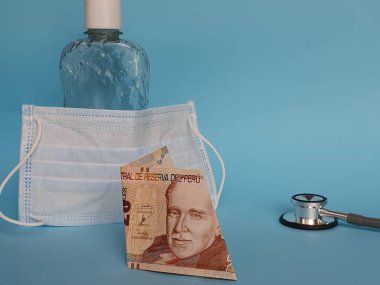 20 tabanlı Peru banknotu, maske, jel alkollü şişe ve mavi arka planda steteskop.