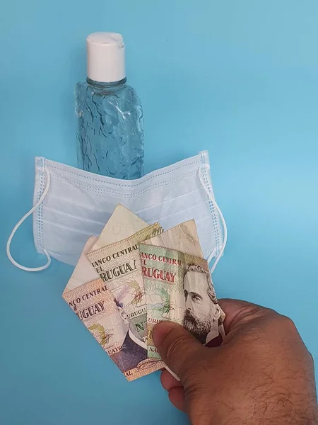 Maske ve bir şişe jöle için uruguay parasıyla ödeme yapan bir adamın eli.