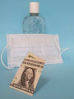 Amerikan 1 dolarlık banknot, maske, jel alkollü şişe ve mavi arka plan.