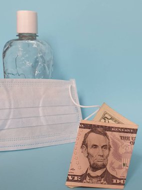 Beş dolarlık Amerikan banknotu, maske, jel alkollü şişe ve mavi arka plan.