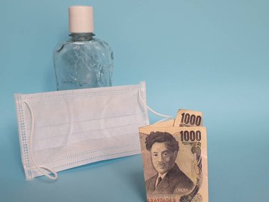 Japon banknotu 1000 yen, maske, jel alkollü şişe ve mavi arka plan.
