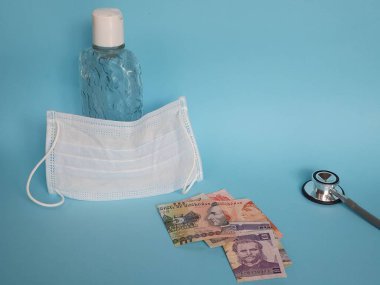 Honduras banknotları, maske, jel alkollü şişe ve mavi arka planda steteskop.