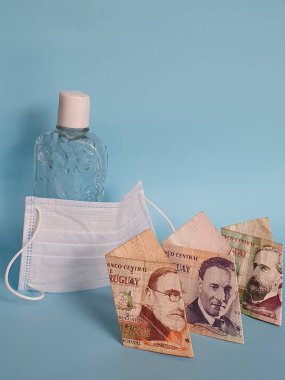 uruguay banknotları, yüz maskesi, jel alkollü şişe ve mavi arka plan