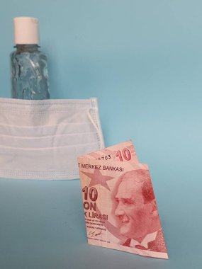 Türk banknotu 10 lira, yüz maskesi, jel alkollü şişe ve mavi arka plan