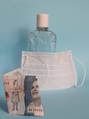 2000 pezoluk Kolombiya banknotu, yüz maskesi, jel alkollü şişe ve mavi arka plan.