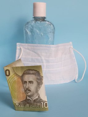 Şili banknotu 1000 peso, yüz maskesi, jel alkollü şişe ve mavi arka plan