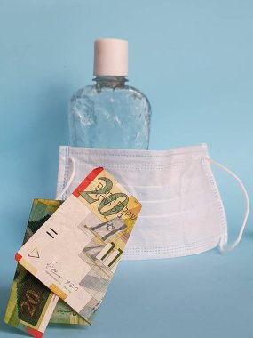 İsrail banknotu yirmi şekel, yüz maskesi, jel alkollü şişe ve mavi arka plan.