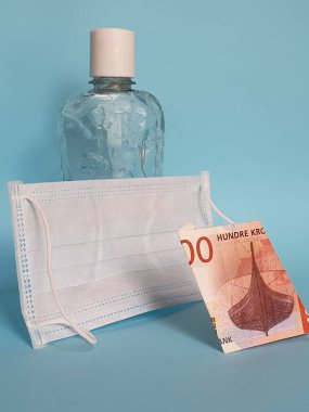 Norveç banknotu 100 kron, yüz maskesi, jel alkollü şişe ve mavi arka plan