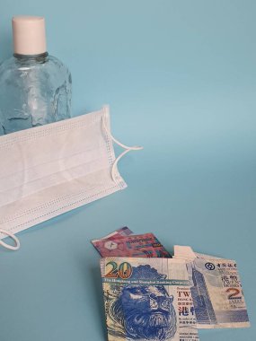Hong Kong banknotları, yüz maskesi, jöleli içki şişesi ve mavi arka plan.