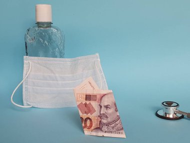 Hırvat banknotu 20 kuna, maske, jel alkollü şişe ve mavi arka planda steteskop.