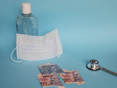 Hırvat banknotları, maske, jel alkollü şişe ve mavi arka planda steteskop.