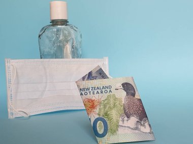 Yeni Zelanda 'da 10 dolarlık banknot, yüz maskesi, jel alkollü şişe ve mavi arka plan.