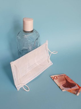 Norveç banknotu 100 kron, yüz maskesi, jel alkollü şişe ve mavi arka plan