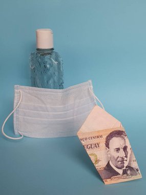 Uruguay banknotu 100 peso, yüz maskesi, jel alkollü şişe ve mavi arka plan