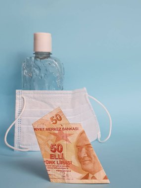 50 liralık Türk banknotu, yüz maskesi, jel alkollü şişe ve mavi arka plan