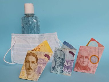 Kosta Rika banknotları, yüz maskesi, jel alkollü şişe ve mavi arka plan
