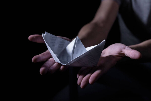Белая бумажная лодка в руках взрослого в темном ключе
