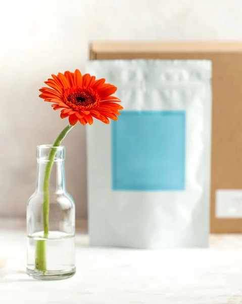 packaging for tea, coffee, solids with a blue label, in the background a craft box, in the foreground a vase with an orange flower