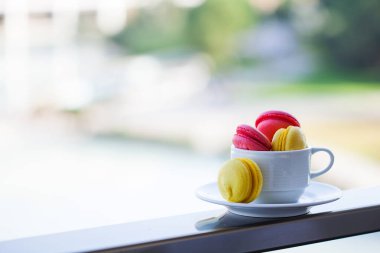 Doğanın arka planında beyaz bir kupada çok renkli hamur tatlısı, metin için yeri olan yatay fotoğraf.