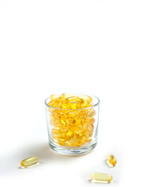 Yellow translucent pills in a glass Cup on a white background. Isolate. Omega, vitamins, food supplements. — Stock Photo, Image