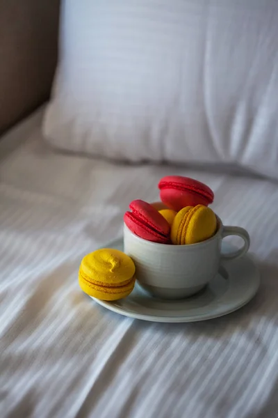 Yataktaki beyaz çarşafların üzerinde beyaz bir daire şeklinde renkli Fransız makaronlu börekler. Kırmızı ve sarı makarna. — Stok fotoğraf