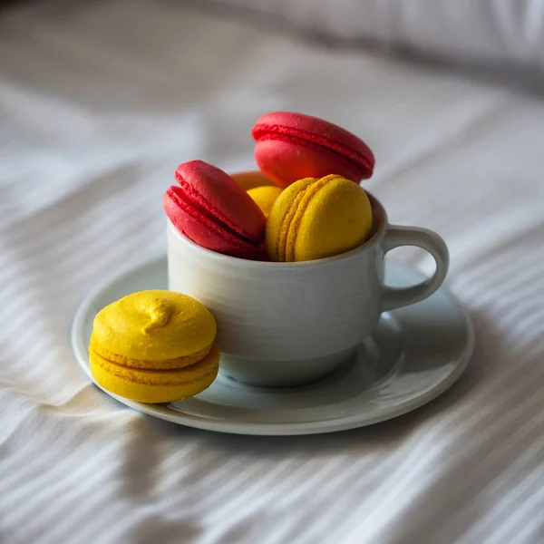 Yataktaki beyaz çarşafların üzerinde beyaz bir daire şeklinde renkli Fransız makaronlu börekler. Kırmızı ve sarı makarna. — Stok fotoğraf
