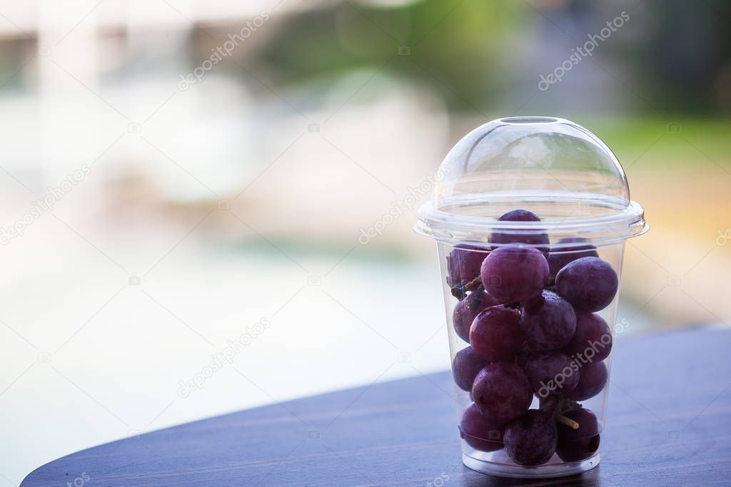 A branch of purple grapes in a transparent plastic Cup on the background of nature with a place for text. A portion of grapes from the buffet.