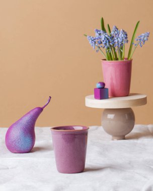 Beyaz masa örtüsünün üzerinde çiçekler, parlak meyveler ve kupalar olan modern bir hayat. Sol üst köşede mesaj için bir yer var, dikey bir fotoğraf. Armut boyası. Tebrik kartı.