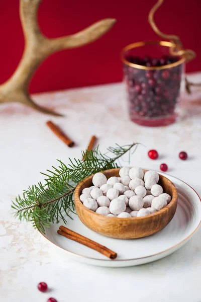 Cranberries in powdered sugar in a wooden plate with a tube of cinnamon and a fir branch. In the background, fresh cranberries and deer horn. — Stock Photo, Image