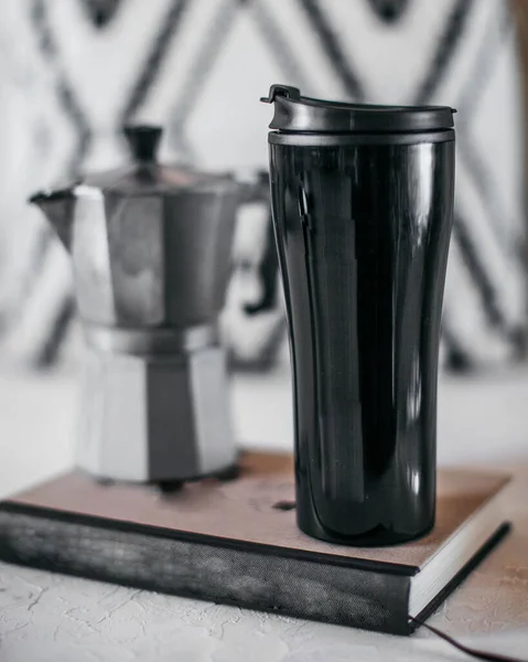 Black thermocup in close-up, with a geyser coffee machine in the background. Vertical photo, the concept of minimalism. — ストック写真